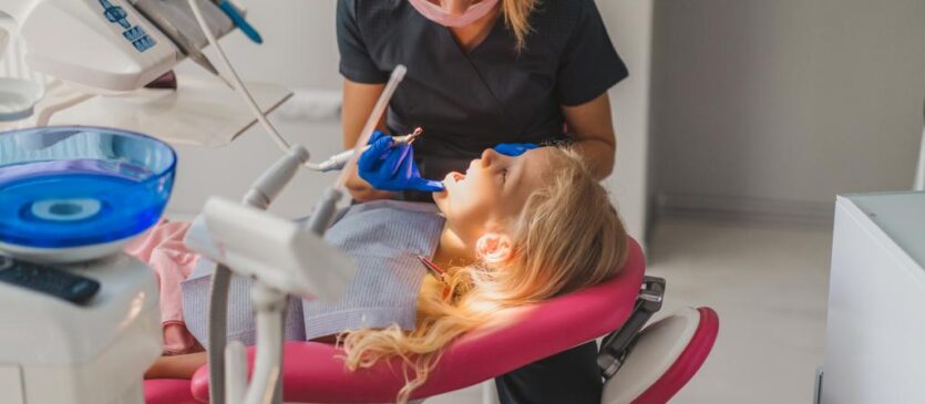 Dentist in latex gloves and medical mask treating little kids teeth